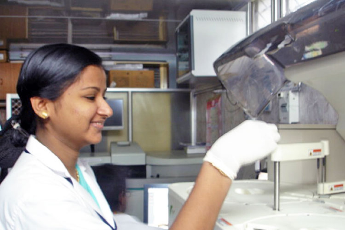 A female lab technician working attentively with advanced diagnostic equipment at Devi Clinical Laboratory.